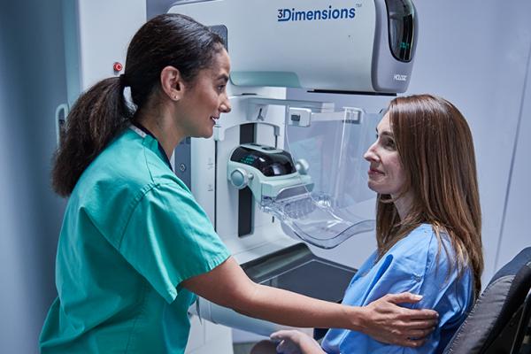 Women sitting in front of a mammography machine with a health care professional at her side.