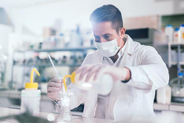 A scientist is carefully pouring liquid from a bottle into a container in a laboratory setting.