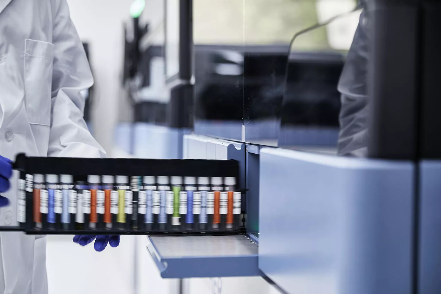 Gloved hand holds rack of vials in lab setting.