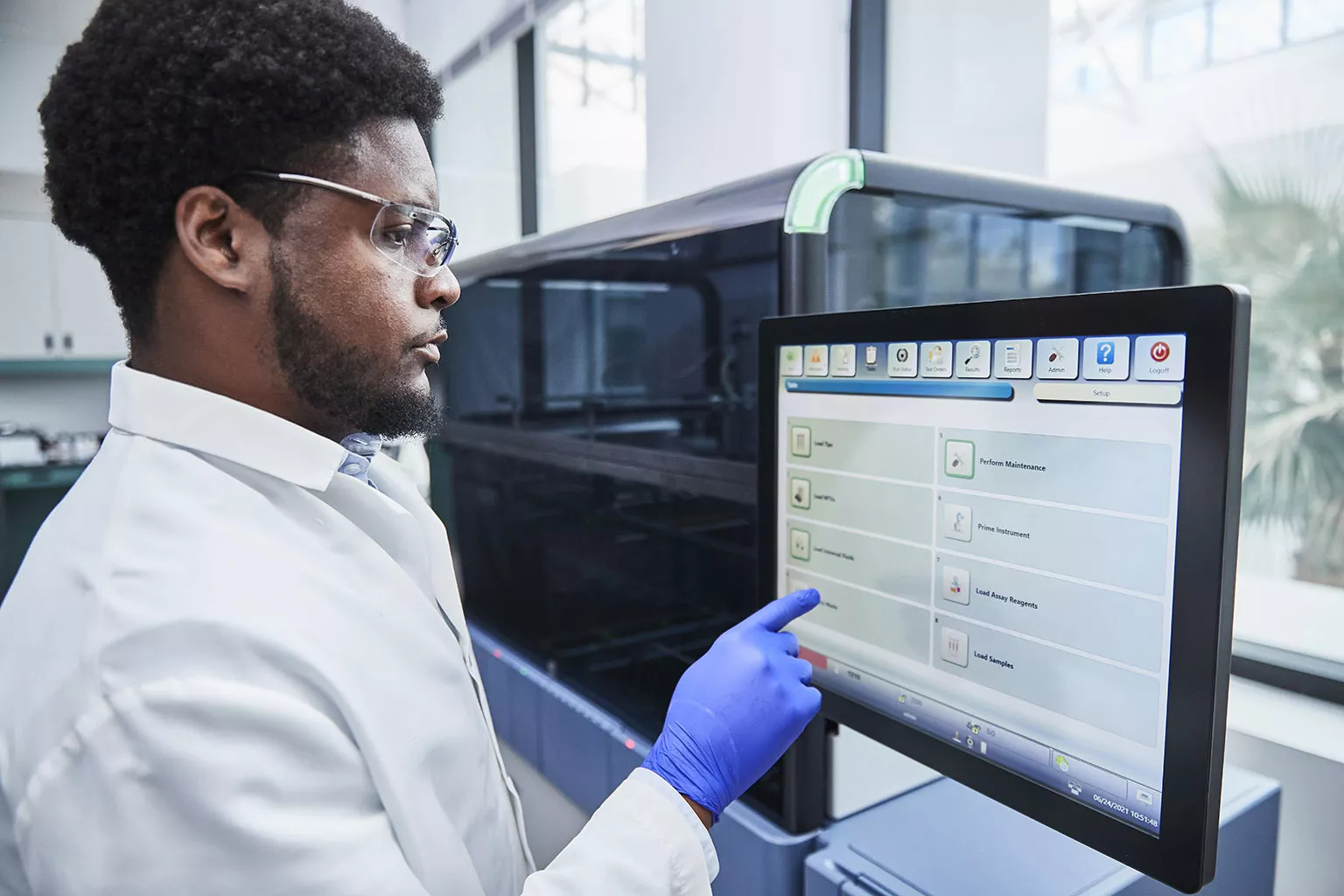 Male physician touching monitor display of Panther System in lab setting.