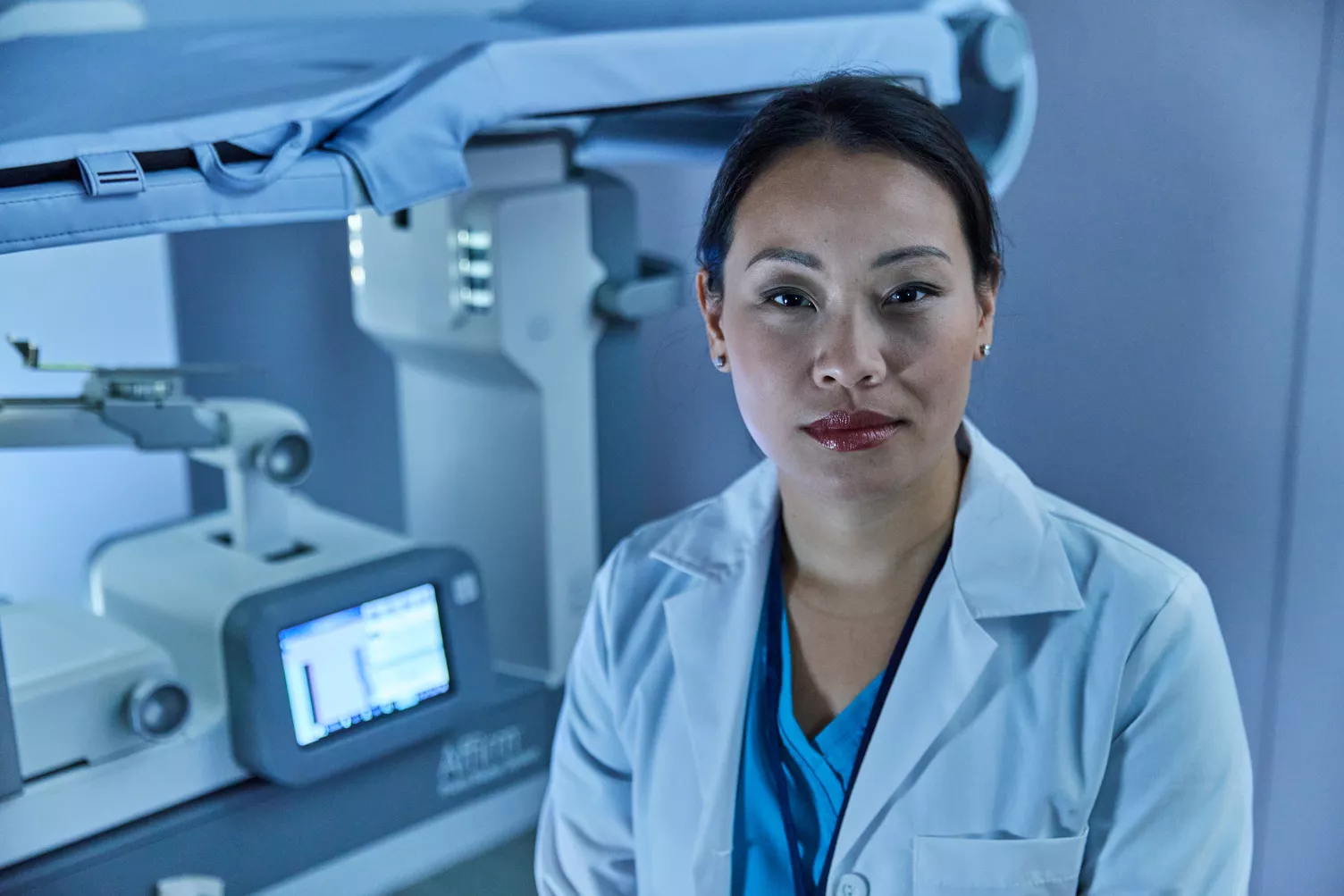 Radiologist looking into camera in front of a Hologic Affirm Prone Biopsy table.