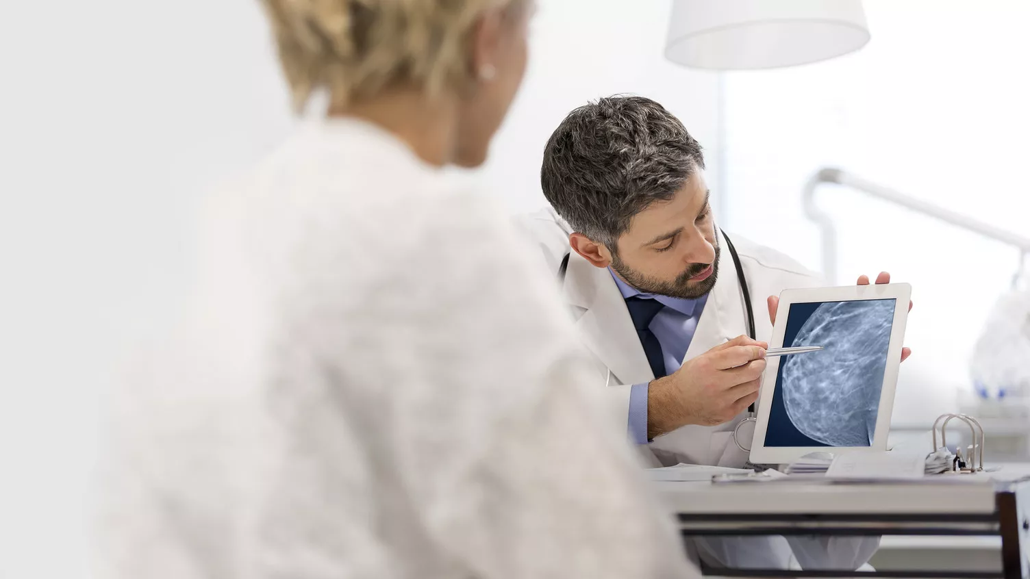 Clinical technician pointing to device to show breast imaging scan